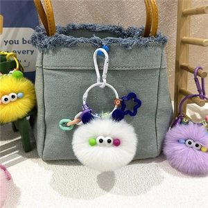 Detail of colorful plush monster keychains with big eyes and letter beads on a denim bag