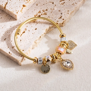 Detail of gold woven bracelet with heart pendant and beads on travertine stone