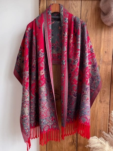 Detail of ethnic paisley shawl with red tassels hanging on a wooden door