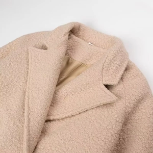 Close-up of beige teddy fur coat collar showing soft curly wool texture and premium stitching