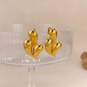 Macro detail of gold layered drop earrings hanging on a textured glass rim