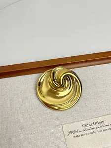 Detailed close-up of a gold-plated whirlpool brooch with polished curved metallic lines