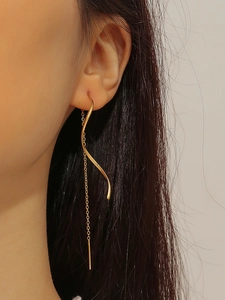 Detail shot of long gold wavy chain earrings on a model showing elegant tassel texture