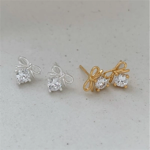 Macro detail of bow-shaped zircon stud earrings in silver and gold finishes