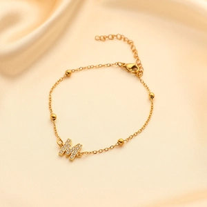 Macro shot of gold stainless steel bracelet featuring crystal pavé M initial and round beads