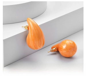 Macro shot of orange marble water drop earrings with gold metal pins on a white pedestal