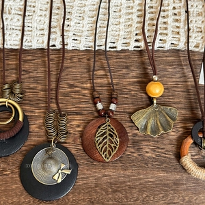 Close-up of bohemian wood bead necklaces with vintage leaf pendants on wooden background
