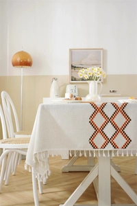 Close-up of cream tablecloth featuring orange geometric embroidery and white fringe detail