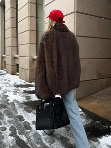 Manteau en fausse fourrure marron avec revers et casquette rouge en rue enneigée