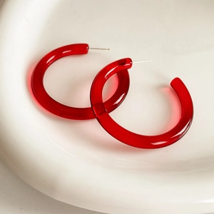 Macro di orecchini a cerchio a C in resina rossa traslucida su un piatto di ceramica bianca