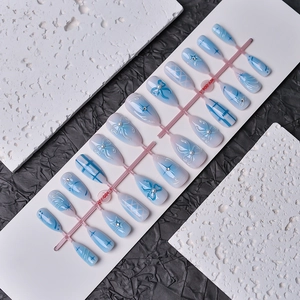 Dettaglio di unghie finte a mandorla sfumate blu con fiocchi 3D e perle eleganti
