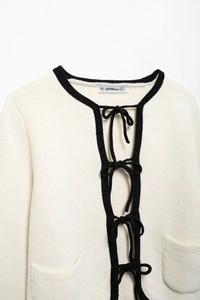 Détail d'un gilet en maille blanc avec bordure contrastée noire, ceinture et poches avant