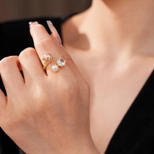 Détail d'une bague dorée ouverte ornée de deux perles et d'un zircon étincelant sur doigt