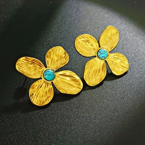 Detailed macro view of golden flower earrings featuring textured petals and turquoise stone