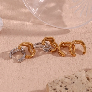 Detailed view of irregular wavy 18K gold and silver ear cuffs on a textured surface
