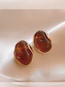 Macro view of irregular amber resin earrings with 18K gold plated edges on silk fabric