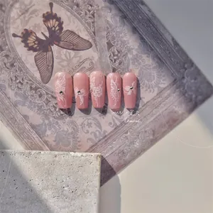 Detail of pink crystal press-on nails featuring white floral and butterfly art with rhinestones