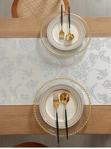 Close-up of elegant dining setting with silver table runner and gold-rimmed placemats