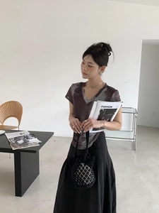 Close-up of model carrying a black woven bucket bag with tie-dye t-shirt and skirt