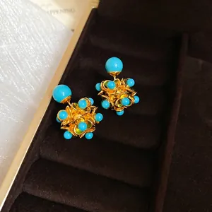 Elegant gold earrings with blue resin clusters and floral pattern on velvet background