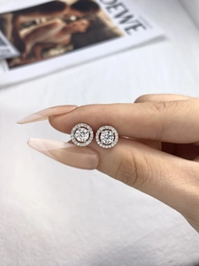 Close-up of elegant silver moissanite halo stud earrings held by a manicured hand