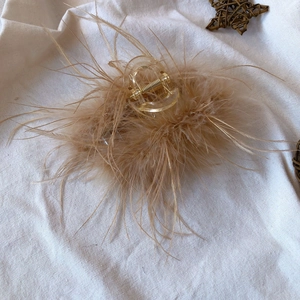 Detailed view of brown ostrich feather hair claw clip on a rustic beige linen background