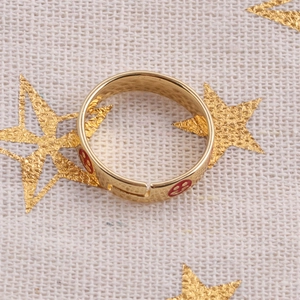 Adjustable gold plated smiling face ring with red enamel icons on white textile