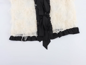 Détail du tissu texturé crème avec bordure en dentelle noire et nœud élégant