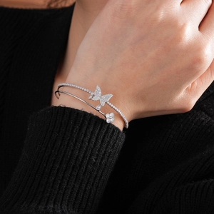 Close-up of a silver-tone double-layered bracelet with zircon butterfly and clover on a wrist