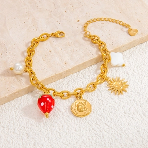 Detail of stainless steel gold bracelet featuring glass strawberry and sun charms