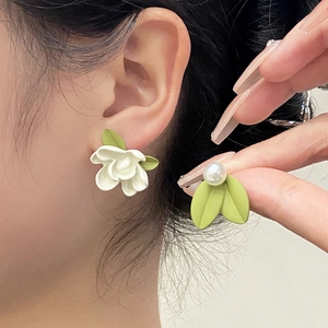 Detailed close-up of floral earring with white petals, green leaf, and a single pearl
