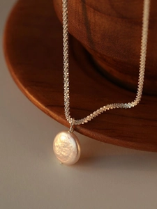 Detailed shot of twisted silver chain with baroque pearl on dark wooden bowl