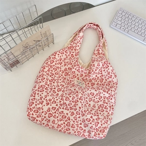 Detail of pink heart leopard print canvas tote bag with woven brand label on white desk