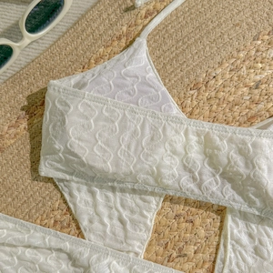 Detail eines weißen Bikinioberteils mit 3D-Wellenprägung und dünnen Nackenträgern