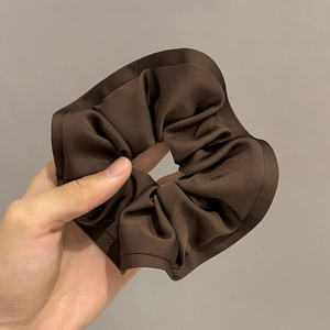 Detailed close-up of dark brown satin scrunchie with elegant pleated fabric texture