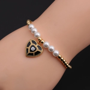 Close-up of evil eye heart pendant on gold beads and white pearl beaded bracelet