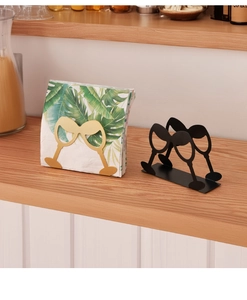 Close-up of wine glass silhouette napkin holders in black and gold on a wooden shelf