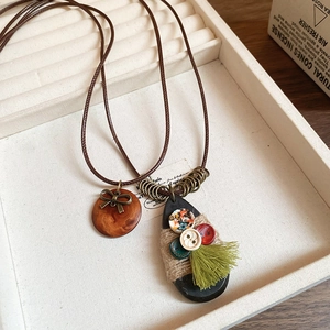 Détail du collier Zen avec pendentif en bois, nœud en métal et pompon vert soyeux