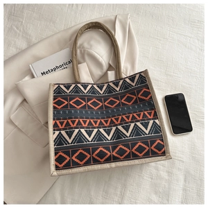 Detail of ethnic jute tote bag featuring orange and black geometric pattern and woven handles
