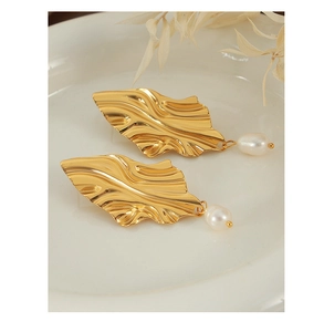 Détail de boucles d'oreilles feuilles dorées avec perles blanches sur plateau céramique