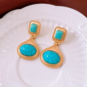 Detail of vintage matte gold drop earrings with green turquoise inlay on a ceramic tray