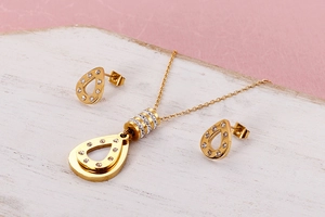 Detail of gold teardrop jewelry set with crystals on a rustic white wood surface