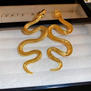 Detailed macro view of gold-tone snake earrings with green rhinestone eyes and scale texture