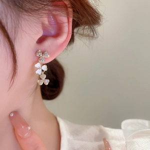 Close-up of elegant gold asymmetric three-flower drop earrings with white shell inlay