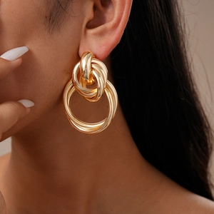Close-up of model wearing gold geometric knotted hoop earrings with a metallic finish