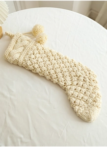 Close-up of cream knit Christmas stocking with decorative pompoms and soft texture