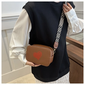 Brown crossbody bag with red heart detail and geometric wide strap on model