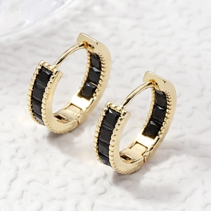Detail of gold hoop earrings with channel-set black square gemstones on white texture