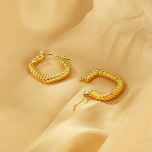 Macro detail of golden twisted rope earrings on silk fabric highlighting metal texture