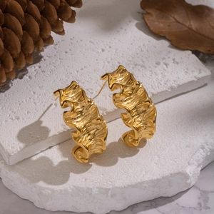 Irregular golden wavy geometric stud earrings on a textured stone with pine cones
